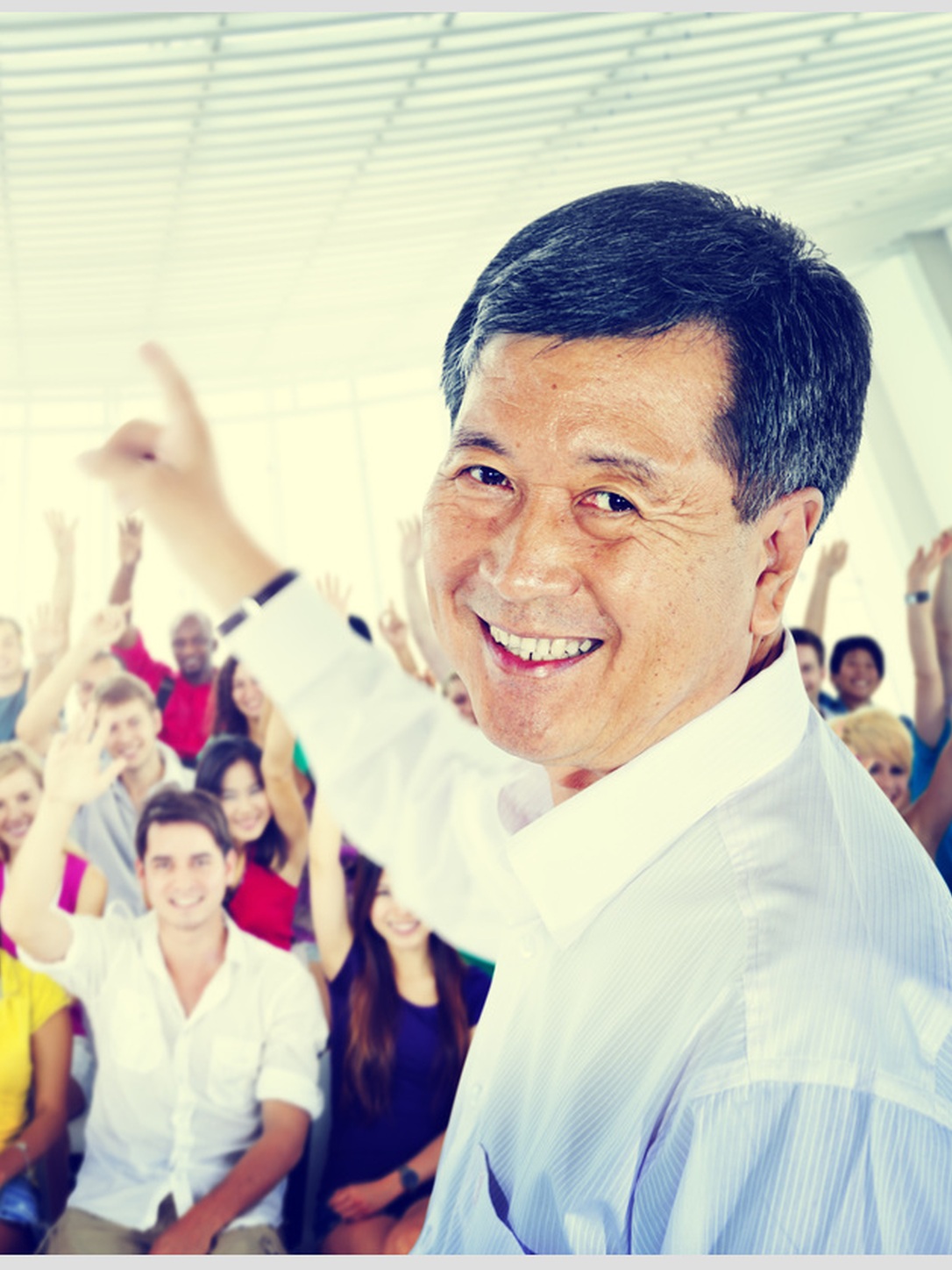 A teacher gestures toward a large class of students raising their hands.