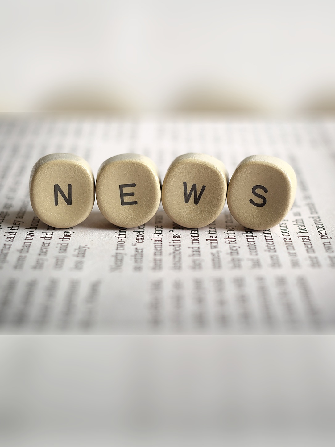 Wooden letter tiles spell “NEWS” on a newspaper.
