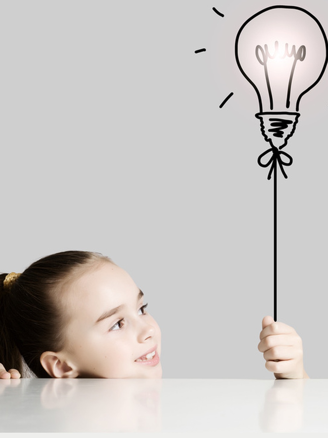 A girl holds a drawn light bulb above her head.