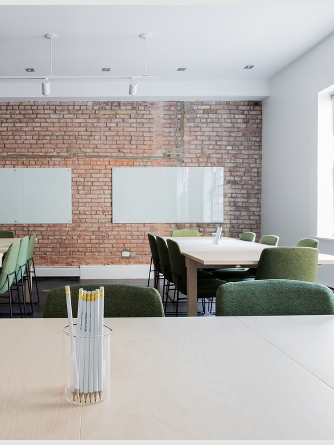 An empty classroom contains tables, chairs, whiteboards, and a cup of pencils.