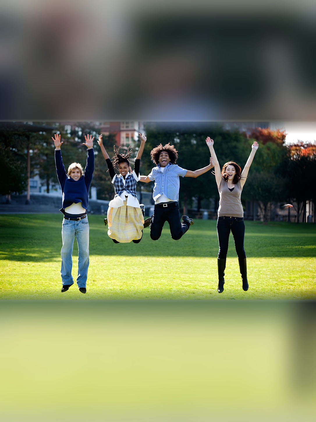 Four students jump with their arms raised in a park.