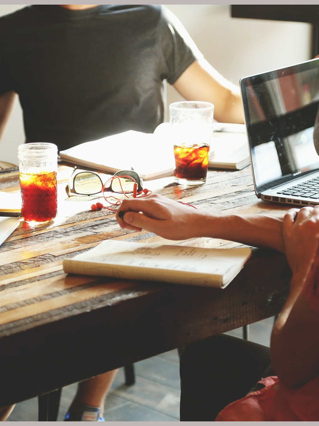 A group collaborates around a table with a laptop, notebooks, and drinks.