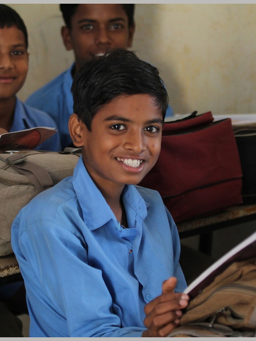 A young student smiles while holding a workbook in class.