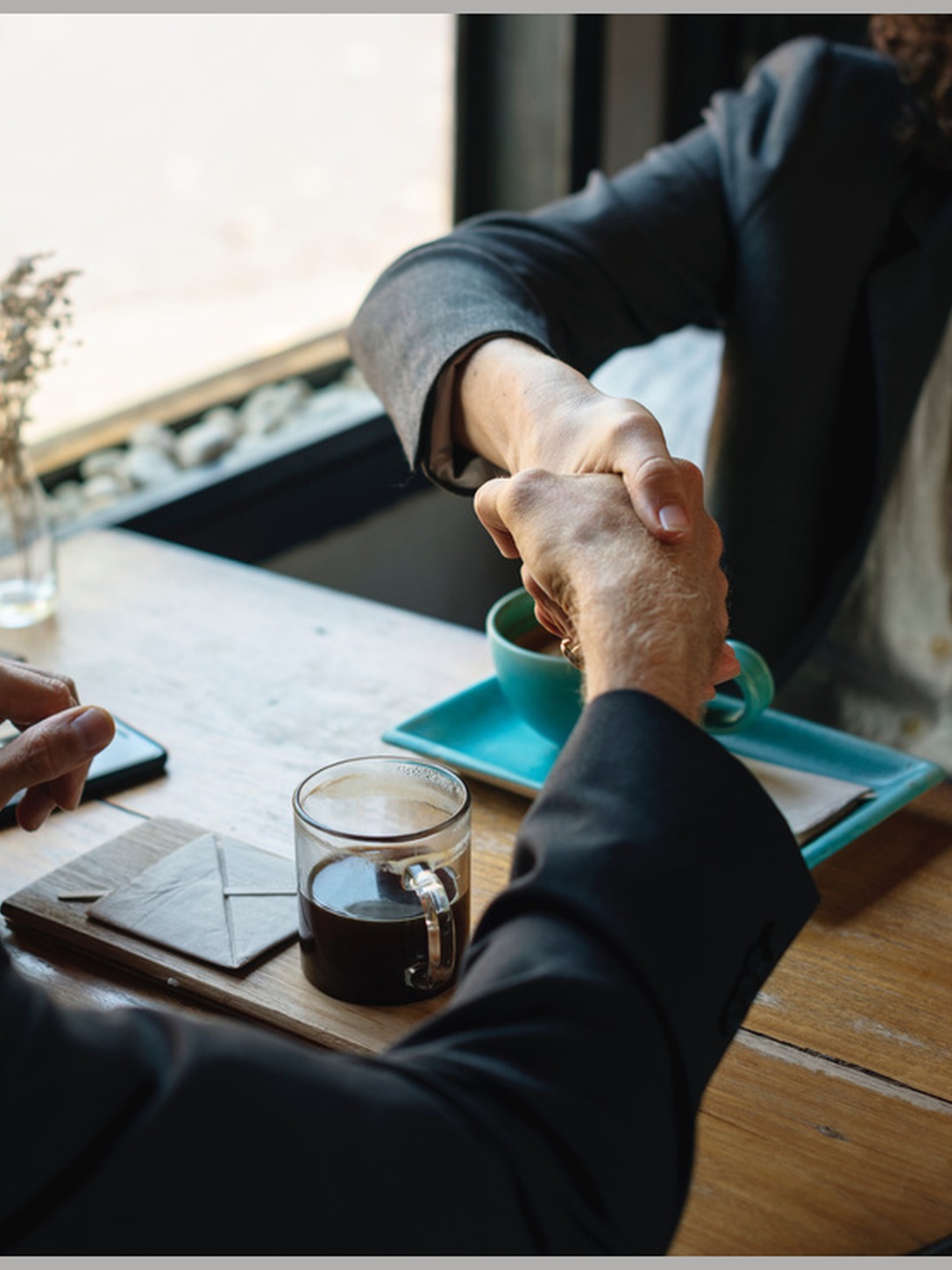 Two professionals shake hands across a café table.