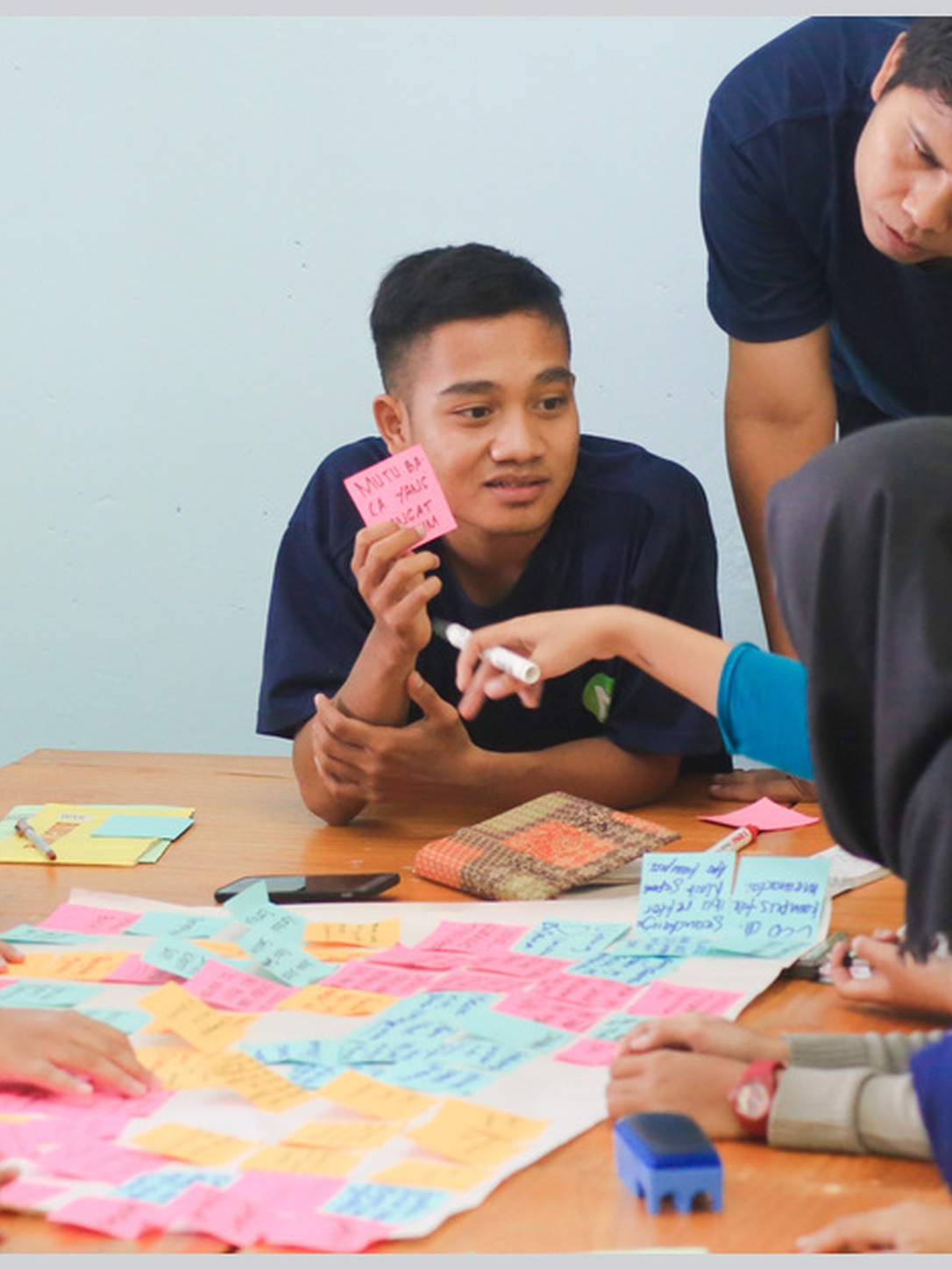 Students brainstorm around a table covered with colorful sticky notes.