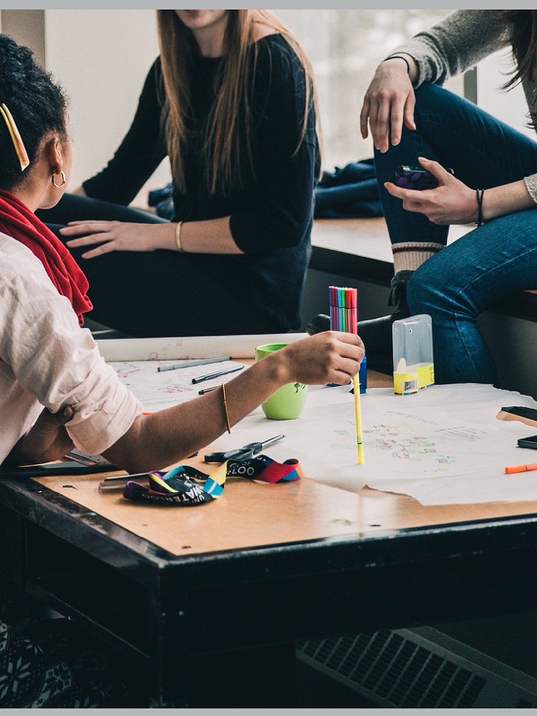 Students collaborate around a table covered with paper and colorful markers.
