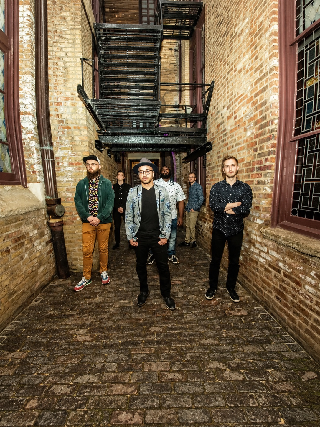 The six members of Bassel and the Supernaturals pose in a brick alley.
