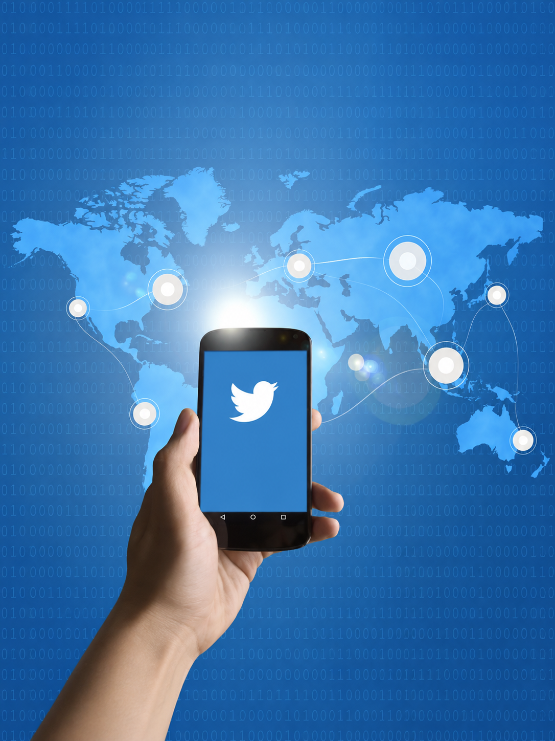 A hand holds a smartphone displaying the Twitter bird logo against a connected world map.