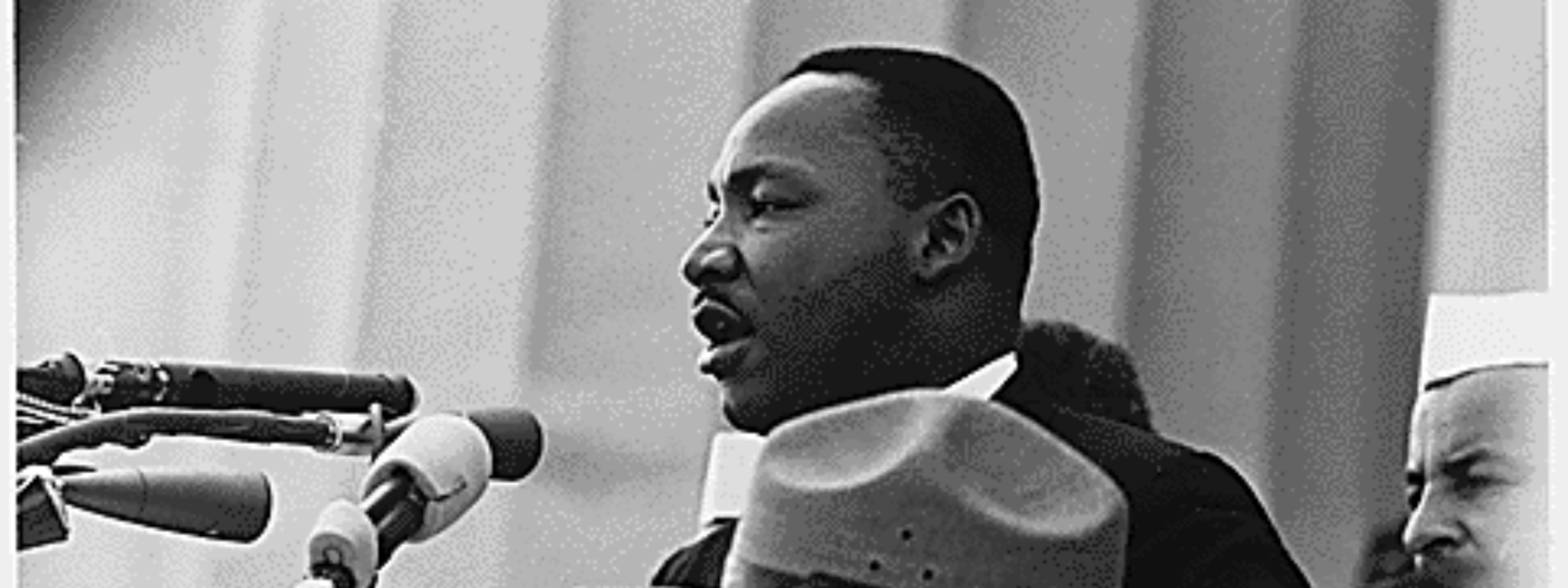 Martin Luther King Jr. speaks into microphones before a crowd.