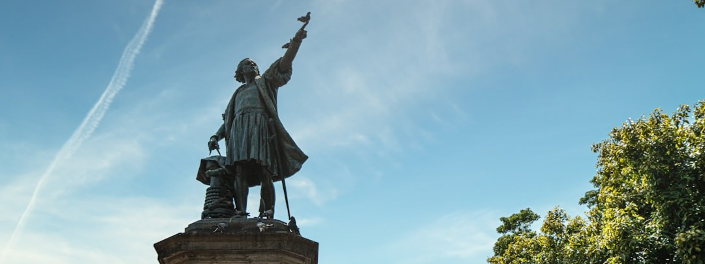 A statue of Christopher Columbus raises one arm against a blue sky.