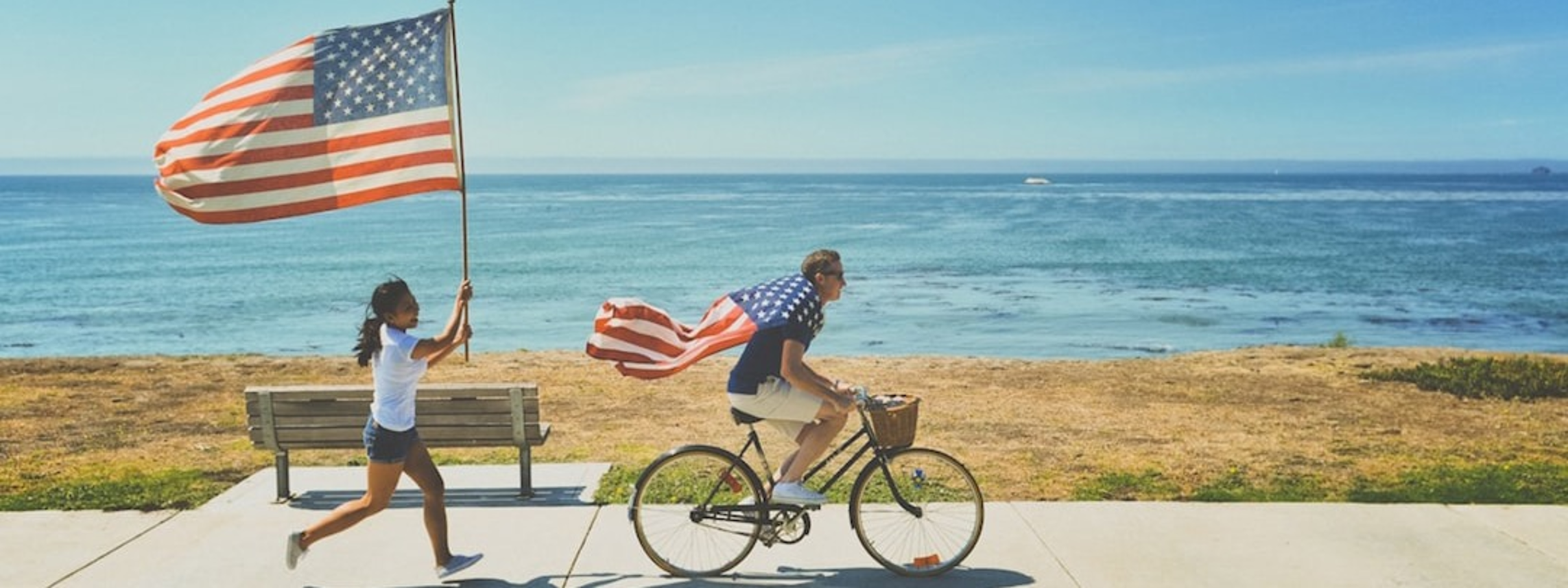 A cyclist draped in a U.S. flag rides along an oceanfront path.