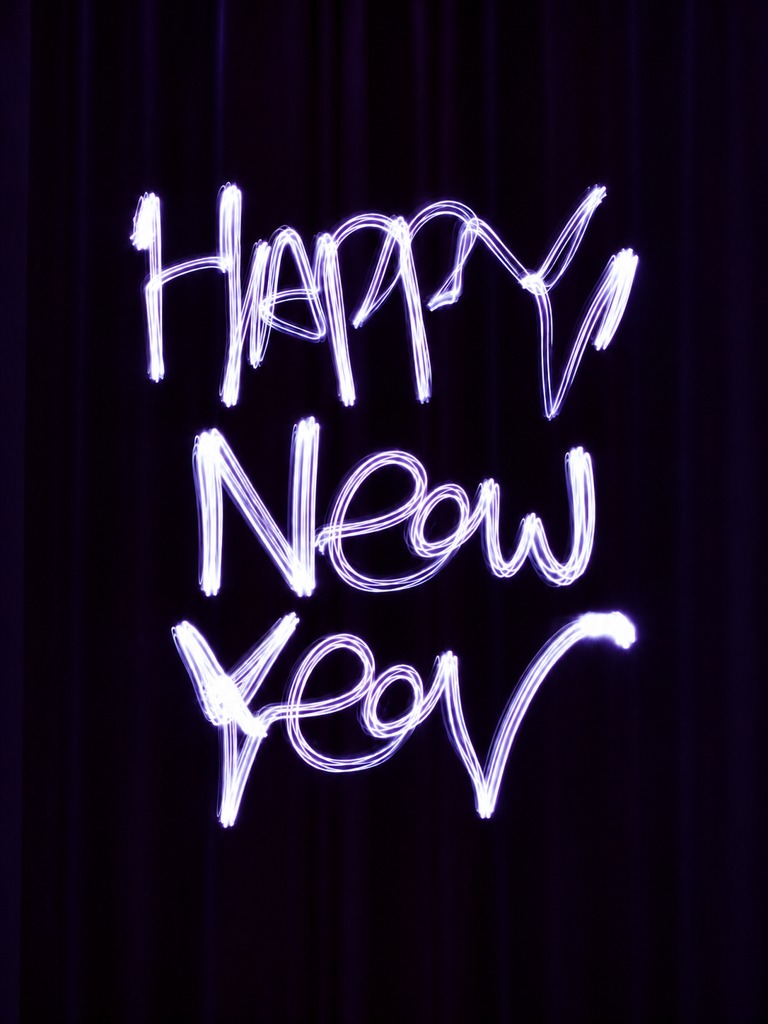 “Happy New Year” written in glowing white and violet light trails on a dark background.