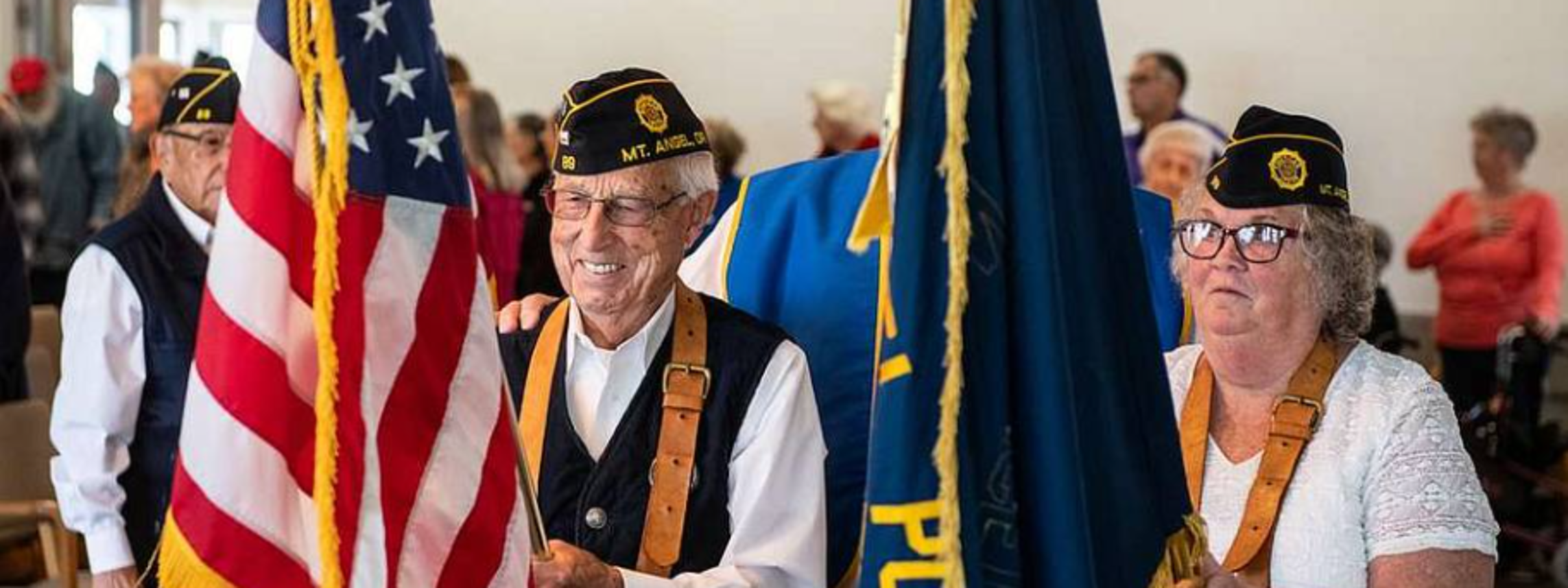 Veterans in military caps carry U.S. and service flags during a ceremony.