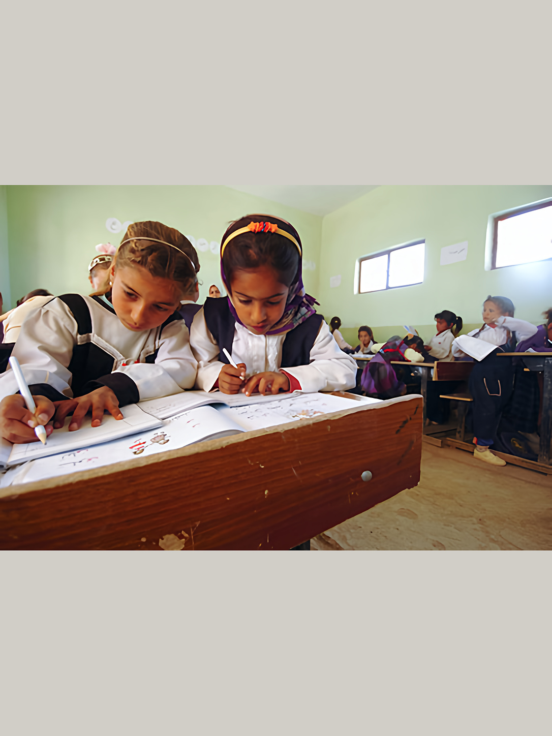 Two schoolgirls work together at a classroom desk.