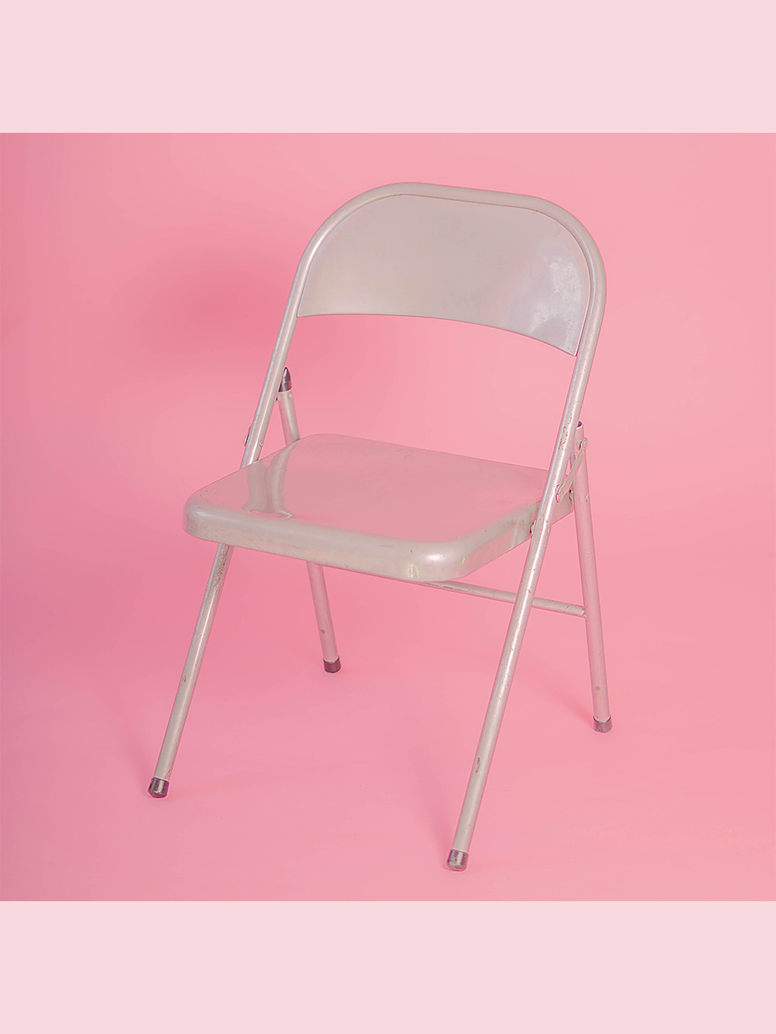 A white folding chair centered against a pink background.